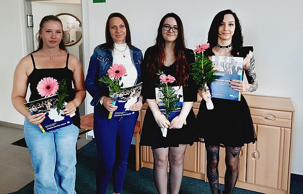 Pflegehelfer*innen in Bitterfeld-Wolfen verabschiedet Eine Mitarbeiterin der Euro Akademie Bitterfeld-Wolfen verteilt die Zeugnismappen an die Absolventinnen und Absolventen, die sich in einer Reihe aufgestellt haben. Eine weitere Mitarbeiterin assistiert.