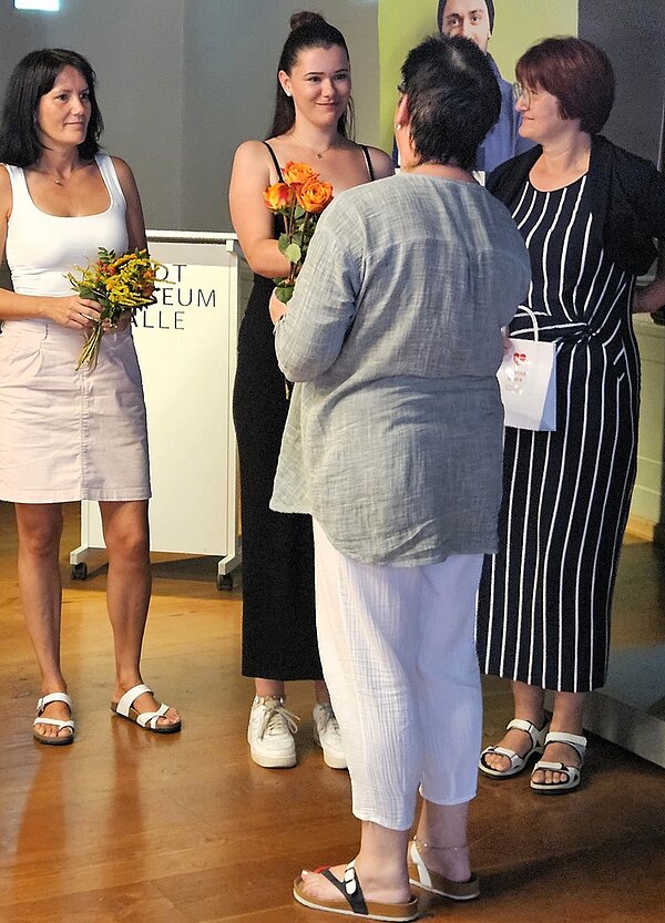 Lehrkräfte überreichen einer Absolventin ihr Abschlusszeugnis und eine Rose. 