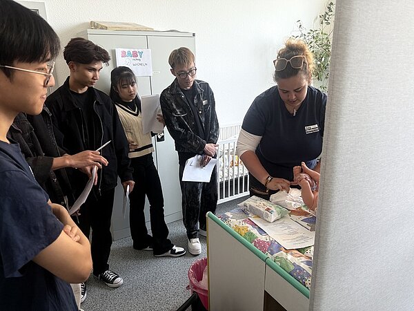 Tag der offenen Tür an der Euro Akademie Bitterfeld-Wolfen Eine Auszubildende zeigt den Besucherinnen und Besuchern anhand einer Baby-Übungspuppe, die auf einem Wickeltisch liegt, das richtige Windeln wechseln und die hygienische Pflege von Babies.
