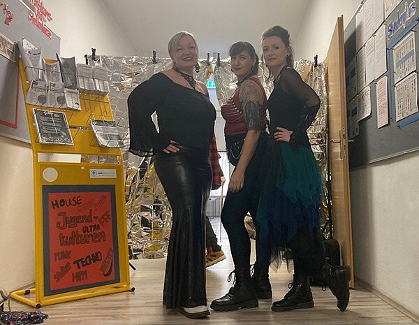 Von Gothic bis Punk! Drei Damen sind als Goths verkleidet, in dunklen Farben, mit Ketten und derben Stiefeln und Make-up.