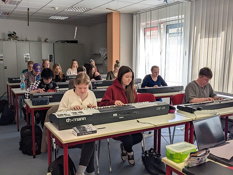 In einem Klassenzimmer sitzen Schüler an Tischen mit Klaviertastaturen.
