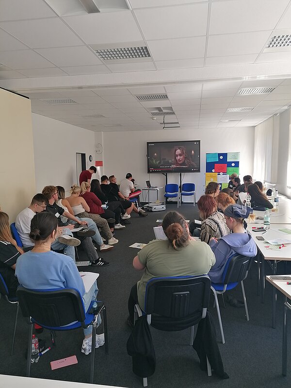 Projekt „Peer-Ausbildung: Schulkino“ durch Alter Gasometer e.V. Zwickau Eine große Gruppe sitzt in einem Seminarraum im Stuhlkreis. Auf dem Bildschirm steht „Peer-to-Peer Ausbildung 2025“.