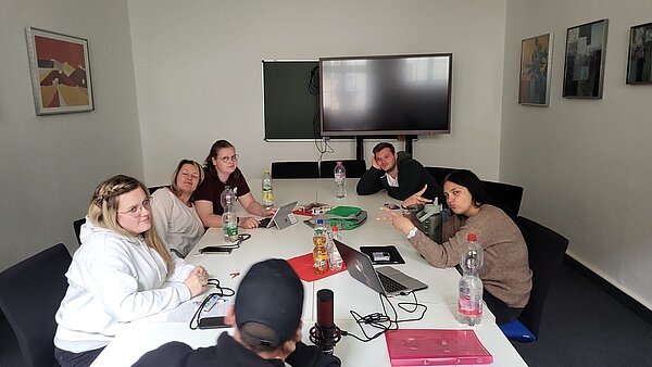 Podcast-Projekt: KAFFEE TRINKEN & SPIELEN Schülerinnen und Schüler der Euro Akademie Halle sitzen an einem Konferenztisch und planen ihr Projekt