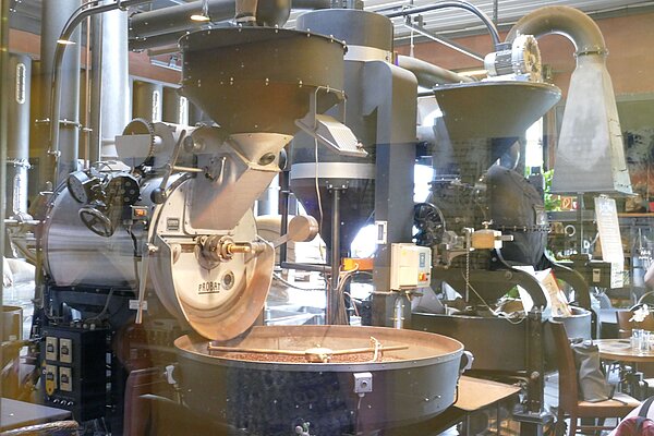Große historische beziehungsweise industrielle Kaffeeröstmaschinen mit Trichtern, Rohren und einer Auffangschale für geröstete Kaffeebohnen.