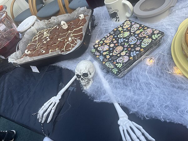 Halloween-Kuchenbasar in der Euro Akademie und den Euro-Schulen in Meißen Blick auf das Kuchenbuffet, das ausgelegt ist mit Spinnennetz-Deko und Skelett, die Kuchen sind gruselig dekoriert.