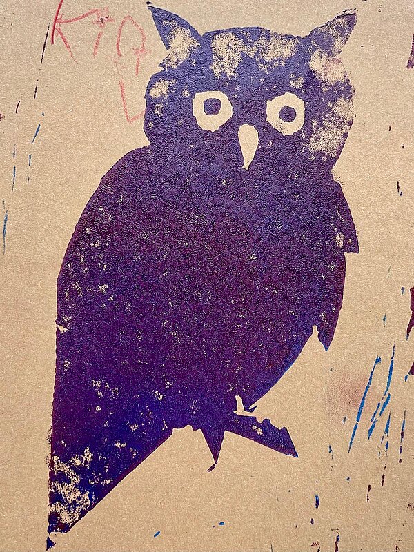 Eulenmotiv als dunkler Druck auf Karton; deutliche Konturen mit Augen und Schnabel, kleine Kritzelspuren am Rand.