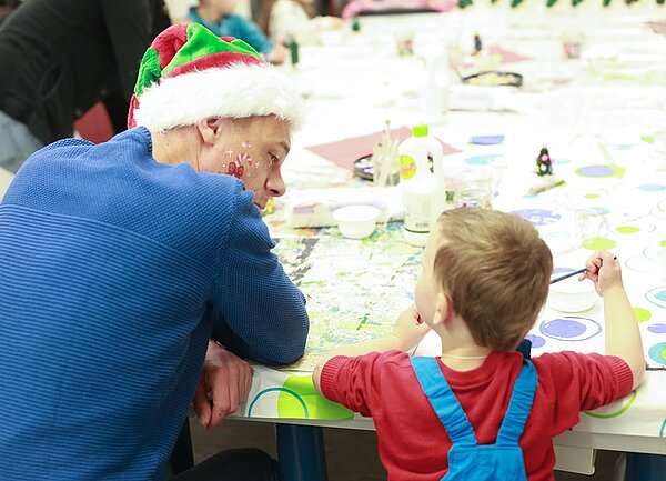 Ein Vater mit Weihnachtsmütze und sein Sohn sitzen an einem Tisch und basteln.