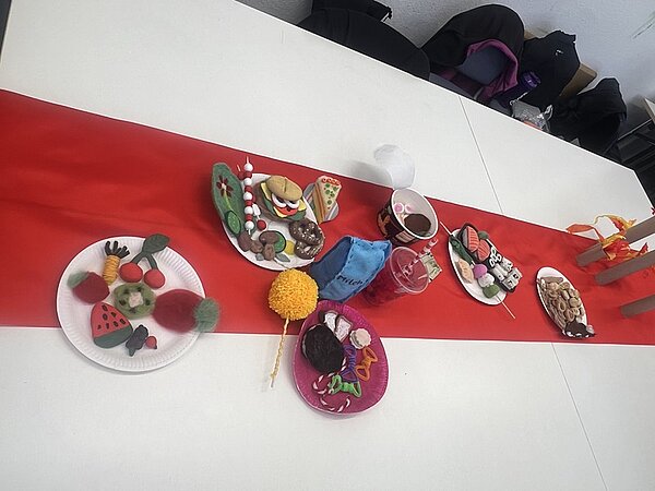 Lange gedeckte Tafel mit rotem Läufer und allen selbst gebastelten und gestalteten Köstlichkeiten der Auszubildenden.