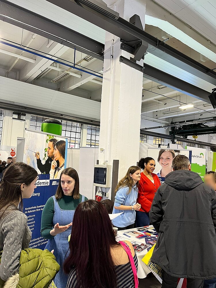 Drei Schülerinnen der Euro Akademie Bamberg unterhalten sich an einem Messestand angeregt mit den Besuchern.