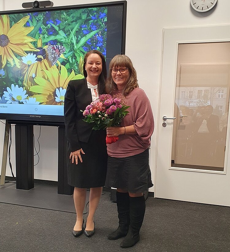 Mitarbeiterinnen der Euro Akademie erhalten einen Blumenstrauß und posieren für ein Foto. 
