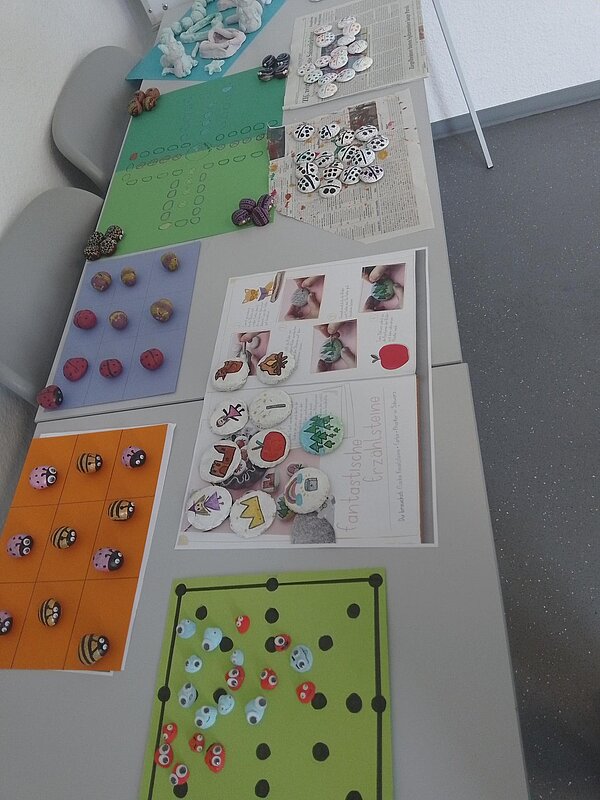 Damit der Herbst nicht zu traurig ist: Unsere Spielempfehlungen Auf einem weißen Tisch befinden sich mehrere selbst gebastelte Spiele. Mensch ärgere dich nicht mit Natursteinen und grünem Spielfeld aus Papier, Mühle aus den selben Materialien und weitere Spieleklassiker.