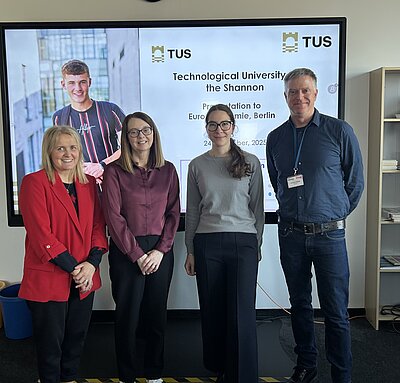 Foto von drei Frauen und einem Mann, die lächelnd vor einer Präsentation der TUS Technological University of the Shannon stehen