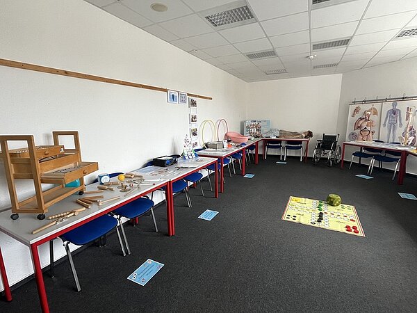 Tag der offenen Tür Im Klassenraum sind die Tische an die Wand gestellt, auf ihnen liegen allerhand Unterrichtsmeterialien, darunter eine lebensgroße Lehrpuppe/Dummy, eine Babybadewanne, ein Rollstuhl steht an der Wand neben einem Platik-Torso.