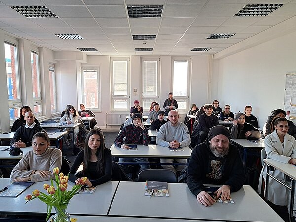 Über 50 neue Azubis gestartet Die neuen Auszubildenden zu Sozialassistentinnen und Sozialassistenten sitzen im Klassenraum an Tischen und posieren für ein Gruppenfoto.