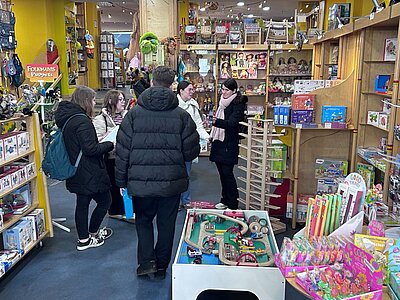 Eine Gruppe von Menschen steht in einem Spielzeuggeschäft und schaut sich gemeinsam Spielwaren an, während sie sich unterhalten.