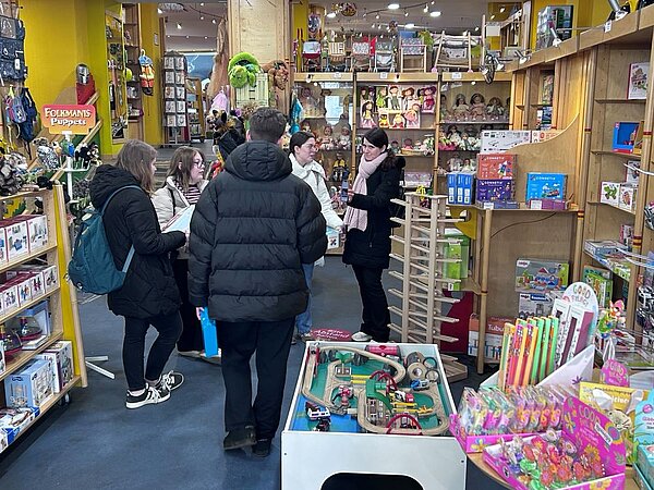 Eine Gruppe von Menschen steht in einem Spielzeuggeschäft und schaut sich gemeinsam Spielwaren an, während sie sich unterhalten.