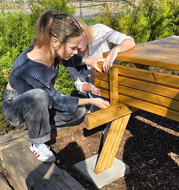 Zwei Schülerinnen schrauben emsig an der hölzernen Bank, die am Holztisch befestigt ist. 