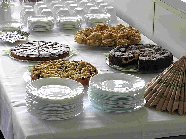 Kuchenbuffet mit verschiedenen selbst gebackenen Kuchen, Tellern, Tassen und Besteck.