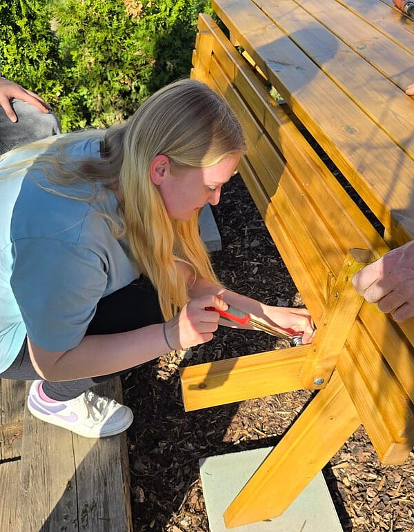 Eine Schülerin schraubt am Holztisch.