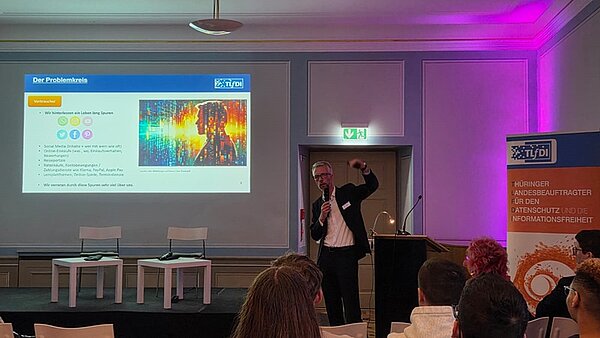 Die Schülerinnen und Schüler sitzen in einem großen Raum und schauen nach vorn zum Referenten und der Präsentation zum Thema Datenschutz.