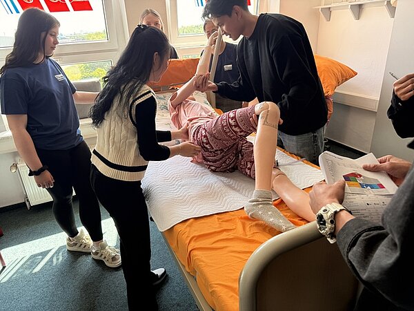 Tag der offenen Tür an der Euro Akademie Bitterfeld-Wolfen Auszubildende und Besucherinnen des Tages der offenen Tür stehen um ein Pflegebett herum, auf dem ein Übungsdummy liegt, und versuchen diesen umzulagern. Eine Übung, um Druckstellen und Wunden bei Patienten zu vermeiden.