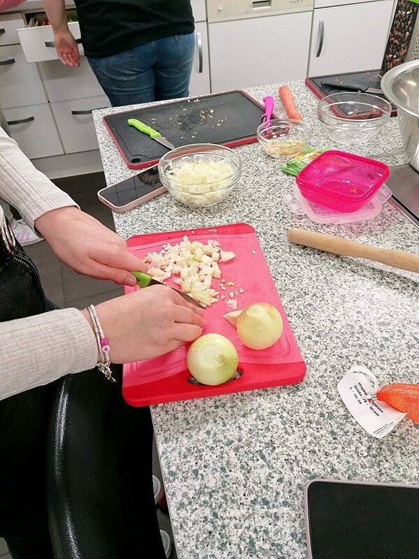An die Töpfe, fertig, los! Auszubildende würfelt Gemüsezwiebeln auf rotem Schneidebrett.
