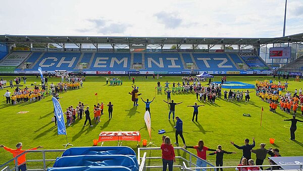 Blick über das Spielfeld des Chemnitzer Stadions, auf dem zahlreiche Kindergruppen gemeinsam mit Betreuungspersonen an einer großen Bewegungsaktion teilnehmen.