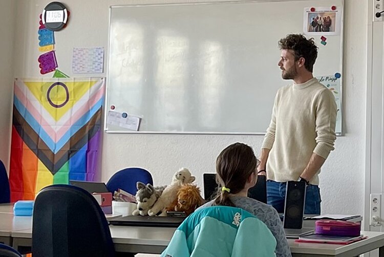 Welche Versicherungen braucht man wirklich? Herr Naun referiert vor der Klasse, im Hintergrund ein Whiteboard und eine bunte Flagge.