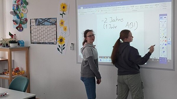 Rundum gelungene Veranstaltung in Meißen Zwei weibliche Auszubildende stehen an einem Whiteboard, auf das Infos projiziert werden und schreiben darauf.
