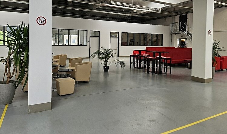 Blick in die Eingangsbereich der Euro Akademie Nürnberg, mit modernen Sitzgelegenheiten und Garnituren in beige und rot, gläsernen Tischen und schönen, groß gewachsenen Pflanzen in sattem Grün.