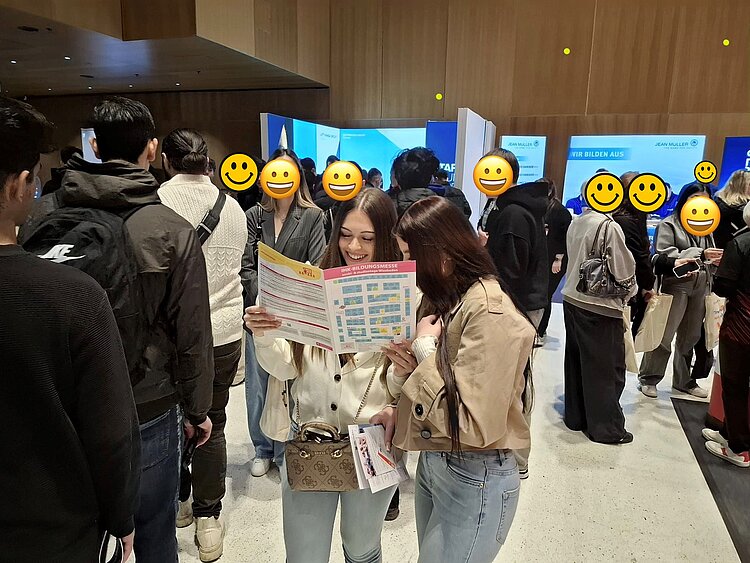 Zwei junge Frauen stehen auf einer Messe und schauen sich einen Katalog an.