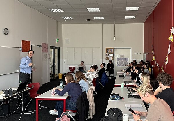 Keine Angst vor KI In einem Klassenzimmer hält ein Mann in einem hellblauen Hemd mit Brille einen Vortrag.