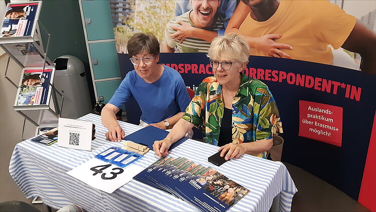 Teilnahme am BIT in Wertheim Zwei Frauen am Infostand der Euro Akademie, nah aufgenommen. Auf dem Tisch liegen blaue Flyer, Kugelschreiber, ein QR-Code sowie ein Schild mit der Nummer 43. Im Hintergrund ein Werbebanner für die Ausbildung „Fremdsprachenkorrespondent*in“ mit dem Hinweis auf Auslandspraktika über Erasmus+.