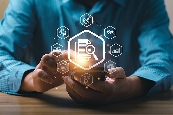 Fortsetzung der Medienbildung im Rahmen von #SouveränDigital Eine Person in einem blauen Hemd hält ein Smartphone in den Händen. Über dem Gerät sind digitale Icons holografisch dargestellt, mit einem zentralen Symbol eines Dokuments und einer Lupe. Weitere Symbole wie ein Globus, eine Zielscheibe, Diagramme, ein Schloss und ein Zahnrad umrahmen das Hauptsymbol. Das Bild symbolisiert Datenanalyse, digitale Sicherheit und Informationssuche im digitalen Zeitalter.