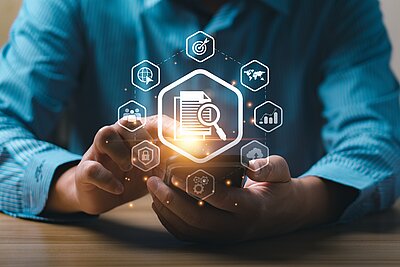  Eine Person in einem blauen Hemd hält ein Smartphone in den Händen. Über dem Gerät sind digitale Icons holografisch dargestellt, mit einem zentralen Symbol eines Dokuments und einer Lupe. Weitere Symbole wie ein Globus, eine Zielscheibe, Diagramme, ein Schloss und ein Zahnrad umrahmen das Hauptsymbol. Das Bild symbolisiert Datenanalyse, digitale Sicherheit und Informationssuche im digitalen Zeitalter.