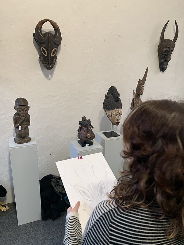 Im Bann der Masken Schülerin zeichnet altes afrikanisches Maskenexponat ab.