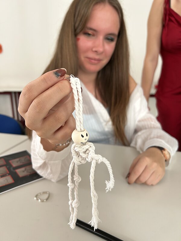 Lernende hält ein kleines Makramee-Gespenst mit Holzkugel-Kopf in die Kamera.