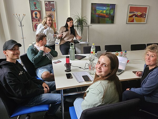 Podcast-Projekt: KAFFEE TRINKEN & SPIELEN Schülerinnen und Schüler der Euro Akademie Halle sitzen an einem großen Tisch und arbeiten an ihrem Projekt