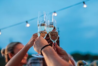 Freudige Gruppe von Personen, die auf einer lebhaften Party auf dem Dach unter funkelnden Lichtern mit Sektgläsern anstoßen.