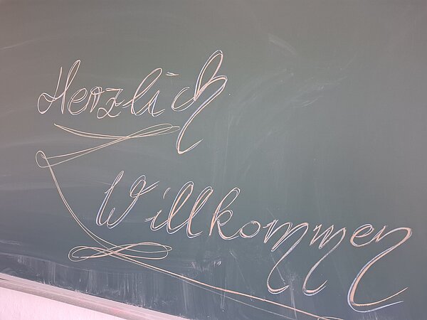 Mit Kreide verzierte Tafel mit dem handgeschriebenen Schriftzug „Herzlich Willkommen“.