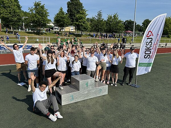 Unterstützung auf Sportveranstaltungen Die Auszubildenden zu Kinderpfelerinnen und Kinderpfleger sowie zu Erzieherinnen und Erziehern der Euro Akademie Pößneck posieren auf der Sportveranstaltung am Sichertreppchen gut gelaunt für ein Gruppenfoto.