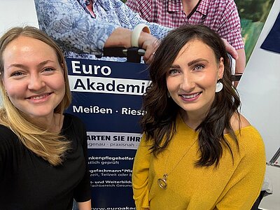Zwei Mitarbeiterinnen der Euro Akademie Dresden stehen lächelnd vor einem Informationsbanner auf dem ‚Tag der beruflichen Schulen‘ im Berufsinformationszentrum (BiZ) am 15. November 2025. Das Banner bewirbt Ausbildungen und Weiterbildungen in den Bereichen Pflege und Soziales. Die Frauen wirken freundlich und aufgeschlossen und repräsentieren die Bildungsangebote der Euro Akademie. Die Szene vermittelt eine einladende und professionelle Atmosphäre.