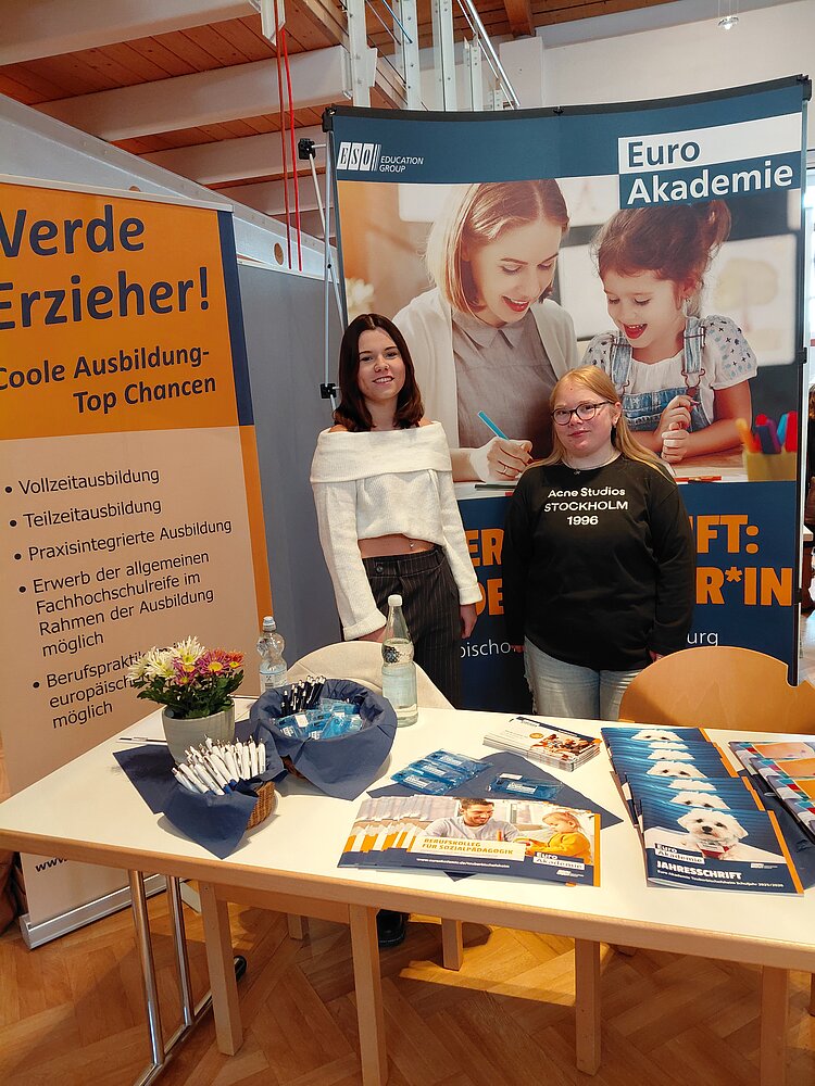 Zwei junge Frauen stehen am Messestand der Euro Akademie Tauberbischofsheim.