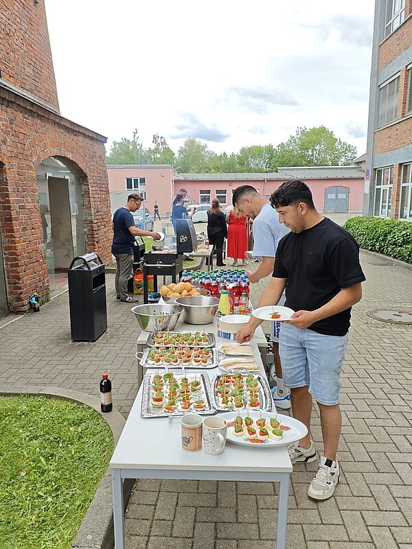Sommerliches Abschlussfest an der Euro Akademie Jena Schülerinnen und Schüler bedienen sich am reichhaltigen Buffet, das auf einer langen Tafel und mit zahlreichen Köstlichkeiten bereitsteht.