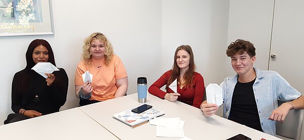 „Die Neuen“ sind da – Euro Akademie Mainz begrüßt neue Klasse der Fremdsprachenkorrespondenten Vier Personen sitzen an einem Tisch und halten stolz ihre selbst gebastelten Origami-Figuren aus Papier in die Kamera.