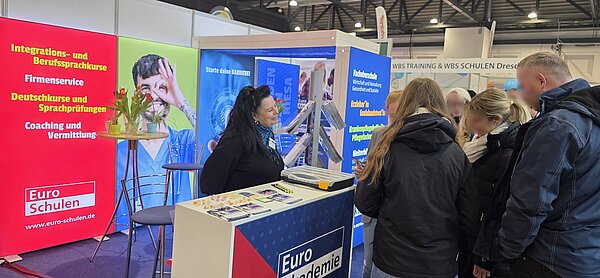 Messestand der Euro-Schulen und Euro Akademie, an dem eine Frau lächelnd eine Gruppe Besucher berät