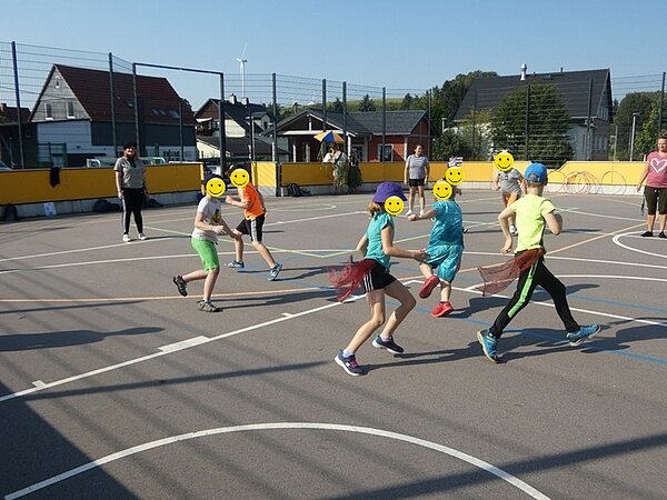 Kinder rennen mit Tüchern an den Hosen über den Sportplatz.