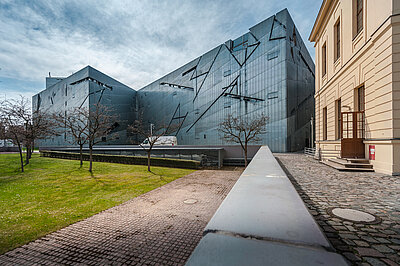 Das Jüdische Museum in Berlin von außen mit den bekannten Glaskacheln und dem vorgelagerten Park.