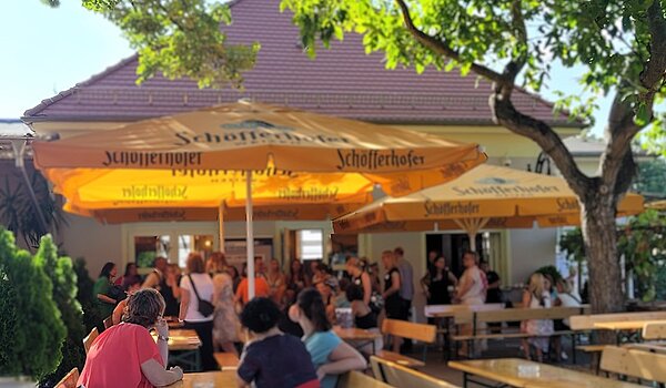 Wiedersehen und Erinnerungen: Ein unvergessliches Alumnitreffen Absolventinnen und Absolventen draußen bei herrlichem Wetter auf Bänken an Tischen unter Sonnenschirmen sitzend.