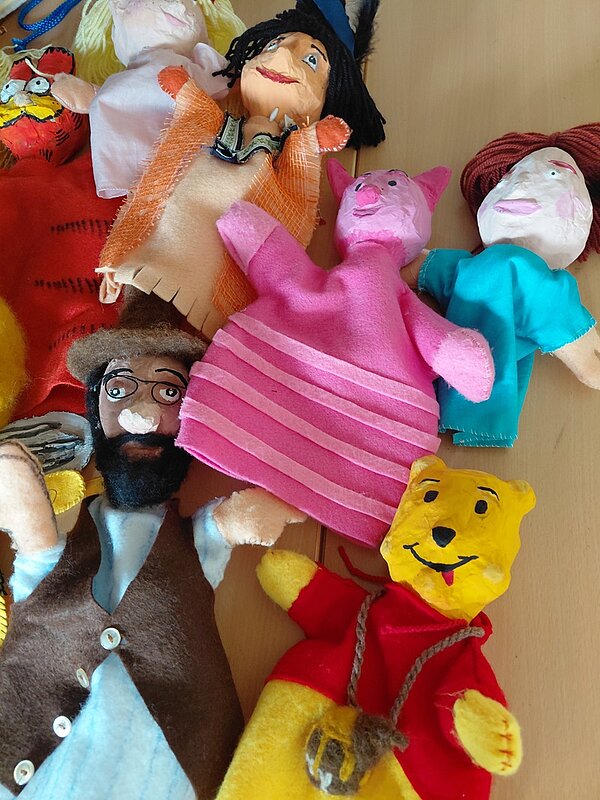 Bunte Handpuppen aus Stoff und Vlies von den Azubis selbst hergestellt liegen auf einem Tisch, darunter ein gelber Bär und eine pinke Puppe mit Ohren.